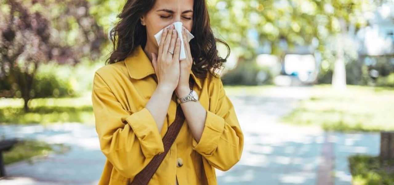 Woman in a yellow spring jacket sneezing into a handkerchief